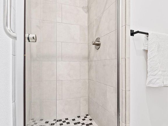 Glass-enclosed tiled shower with a rainfall-style showerhead and mosaic floor for easy-maintenance daily use.