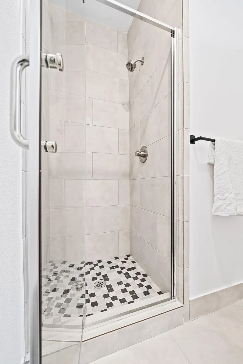 Glass-enclosed tiled shower with a rainfall-style showerhead and mosaic floor for easy-maintenance daily use. - Carver Ave