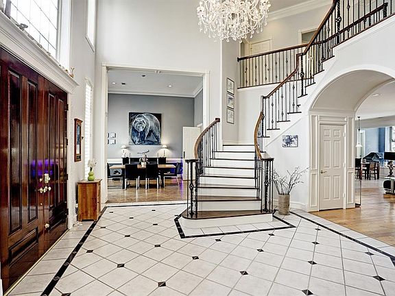 Enter through the double doors with oversized transom window to the two story foyer with so many stunning features which includes tile floor with granite inserts, crystal chandelier, curved wooden stairwell with wrought iron spindles, and with great 