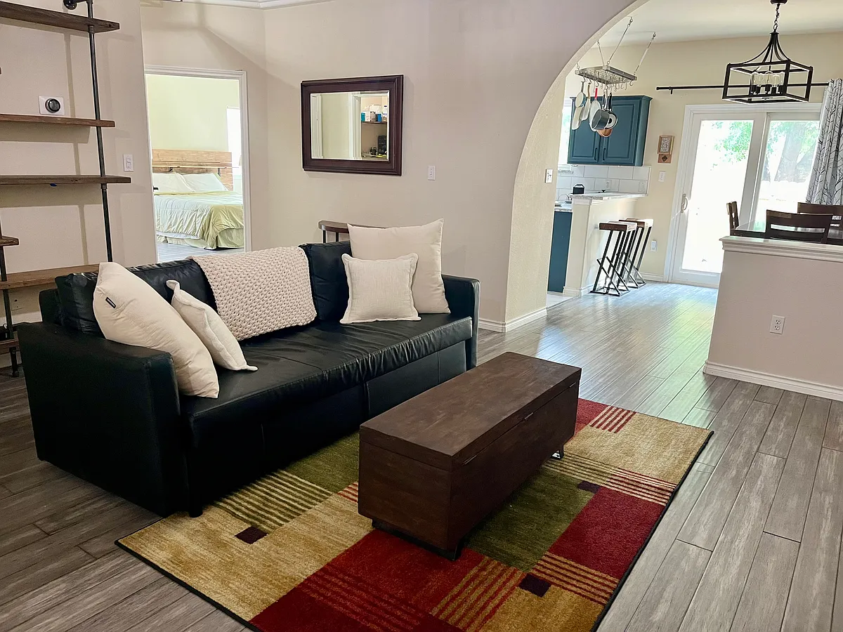 View of living room from the front door. Custom industrial pipe bookshelves + nest located black couch. Coffee table is a wood stained chest. Hanging cherry wood mirror + small credenza slightly shown. - 12269 Abbey Glen Ln