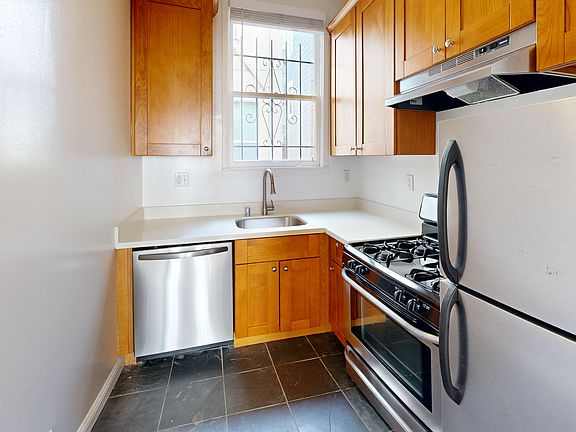Kitchen with multiple cabinets, refrigerator, stove, range hood, and sink