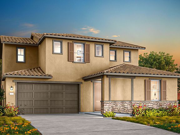 A two-story Mediterranean-style house with a tiled roof, a garage door, and a landscaped yard with c