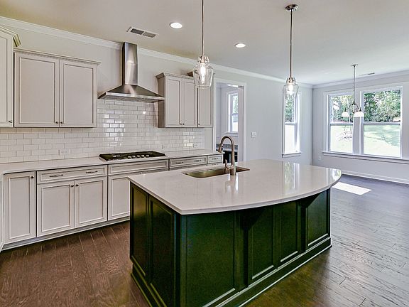Large, open kitchen with white counters cabinets, large curved island with sink and stainless stee