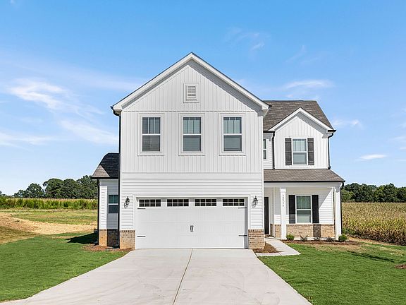 A white house with a garage and a driveway is sitting on top of a lush green field.