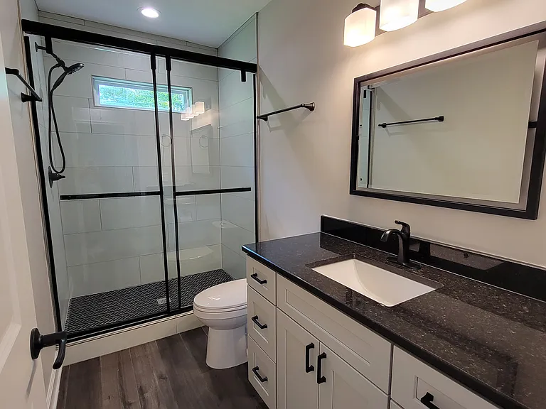 Bathroom -- granite countertops, soft-close cabinets, tiled shower with sliding glass doors, and adjustable shower head.