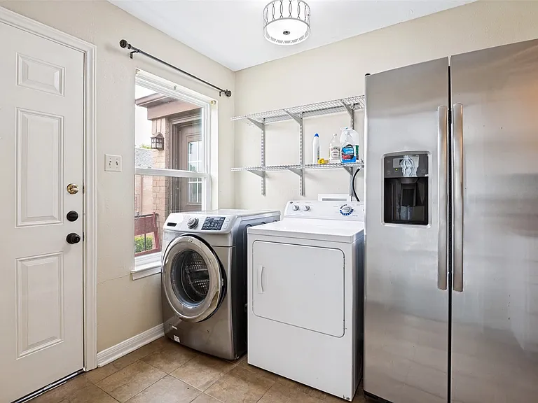 Utility area featuring a side-by-side stainless steel refrigerator with a water and ice dispenser, a front-load washing machine, and a top-load dryer