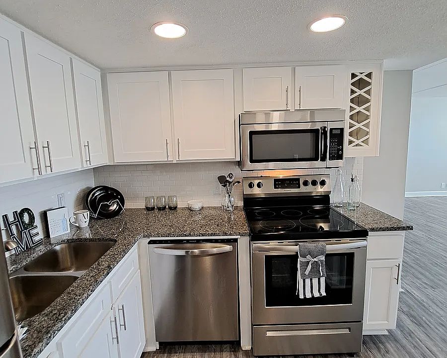 Kitchen equipped with Stainless steal refrigerator, electric stove, microwave, granite countertops, white subway tile and white shaker cabinets.