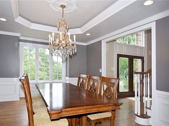 Impressive formal dining room has classic wainscoting, neutral paint and is topped with a tray ceiling, medallion and sparkling 