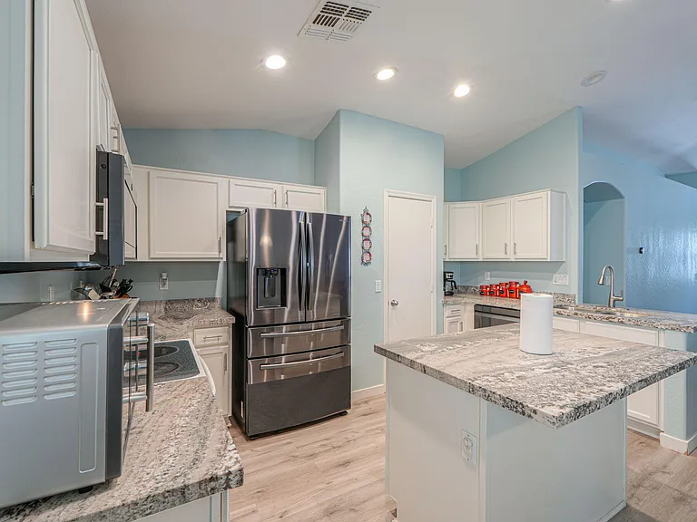 Open kitchen with ample white cabinetry, granite-look counters, center island, and stainless refrigerator with ice/water.