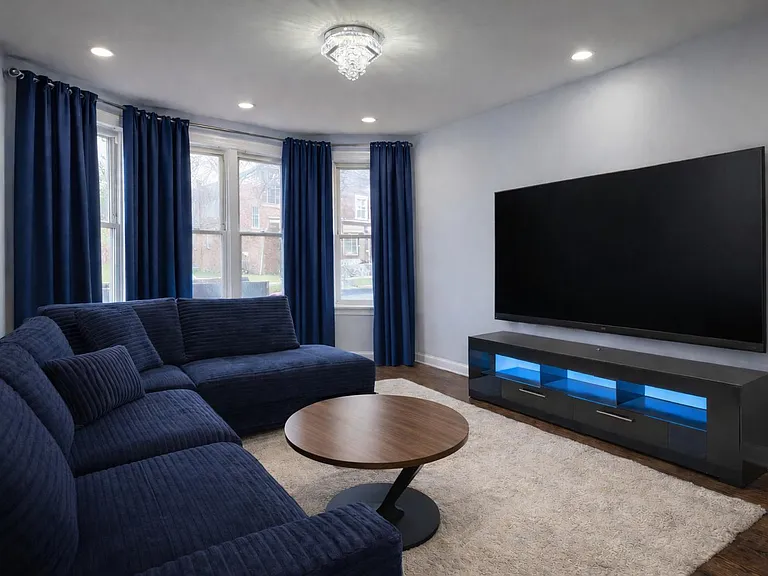 Living room entertainments center features a 70 inch smart Tv, dimmable recess lights, and a beautiful bright chandellier!
