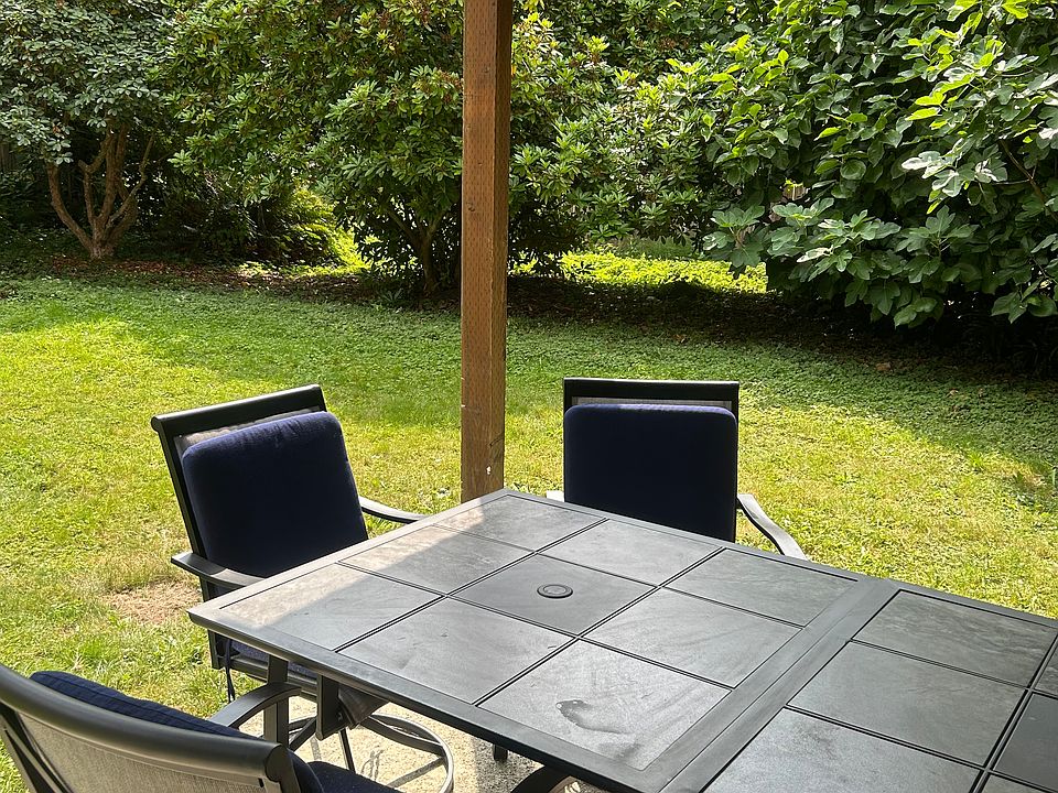 Patio with tables/chairs, lawn and trees. Trees provide beauty and privacy.