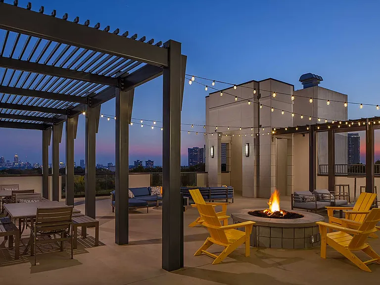 Dusk shot of rooftop fire pit with string lighting and tables and chairs