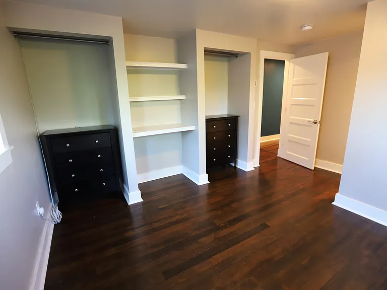Bed 1. Built-in shelves and open closets on left wall with door to hallway. Entrance to closet hidden from view.