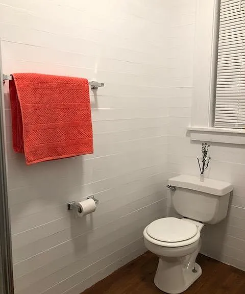 3/4 bath on main floor has shiplap style painted wood walls, toilet, vanity with sink and corner shower.