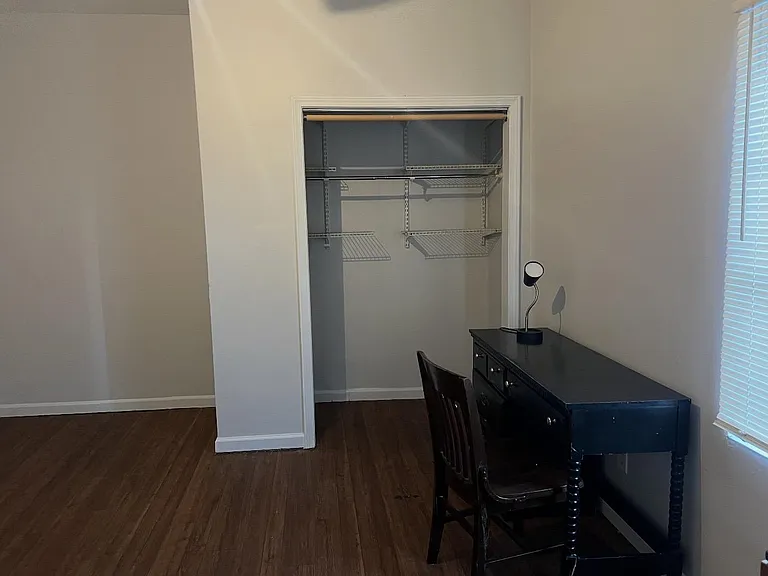 Bedroom includes an open closet with wire shelving, wood-look flooring, and a window with blinds for natural light.