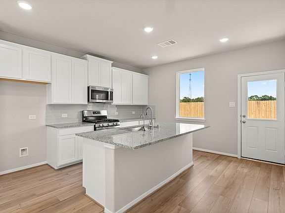 The light and bright kitchen features a large center island, white cabinetry and a modern tile backs