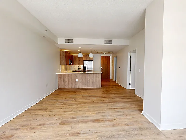 Apartment kitchen with stainless steel appliances, dining and living room with wood-style flooring.