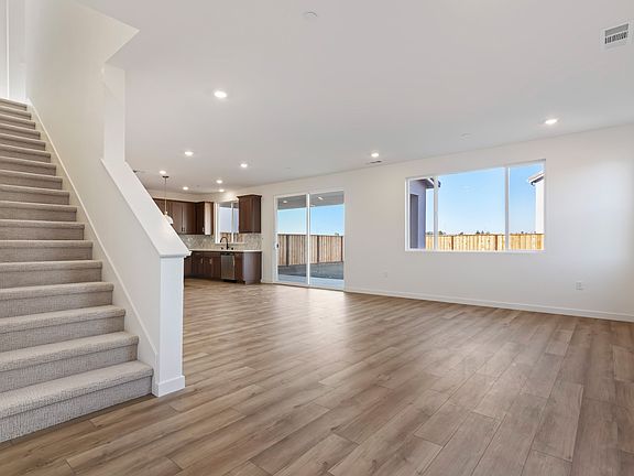 A spacious, open-concept living area with a staircase leading to an upper level, hardwood flooring,