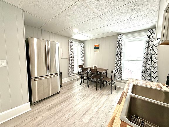 This fully equipped kitchen boasts a sleek French door stainless steel fridge and a dining area with a table, chairs, and a cozy corner bench, perfect for meals and gatherings.