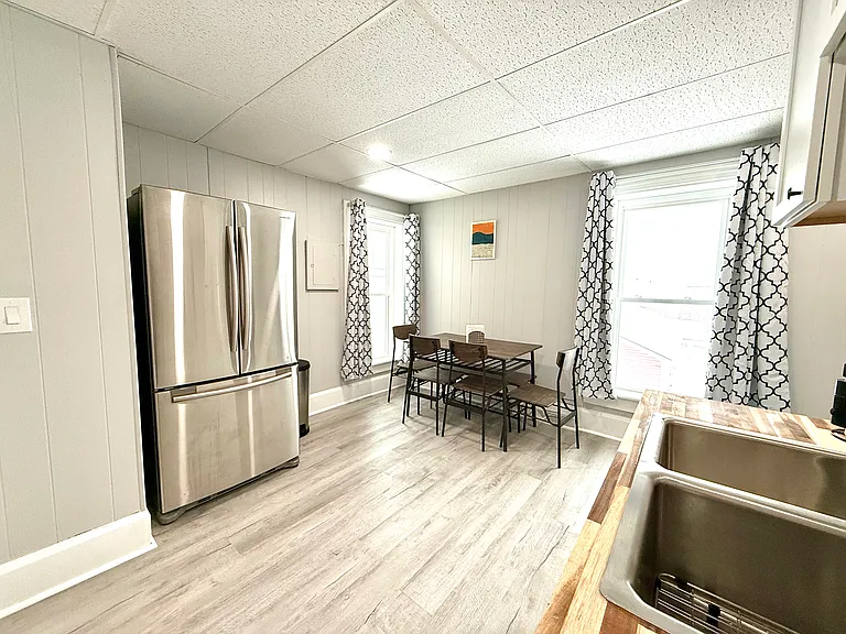 This fully equipped kitchen boasts a sleek French door stainless steel fridge and a dining area with a table, chairs, and a cozy corner bench, perfect for meals and gatherings.