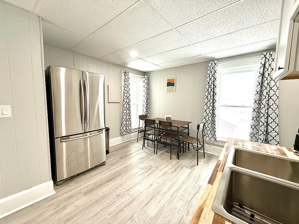 This fully equipped kitchen boasts a sleek French door stainless steel fridge and a dining area with a table, chairs, and a cozy corner bench, perfect for meals and gatherings.