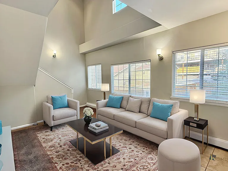Bright and inviting living room with high ceilings, natural light, elegant decor, and cozy seating with stylish blue accents.