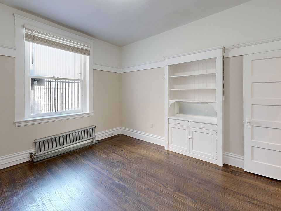 Cozy room with hardwood floors, a large window, a radiator, and a built-in shelf