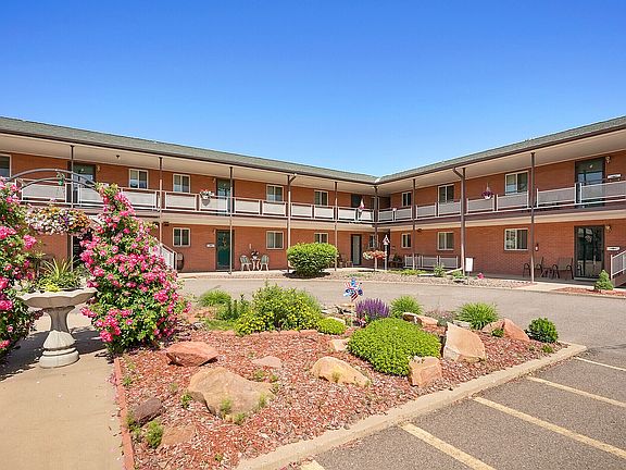 Charming brick apartment complex with a beautifully landscaped courtyard featuring vibrant flowers and lush greenery.