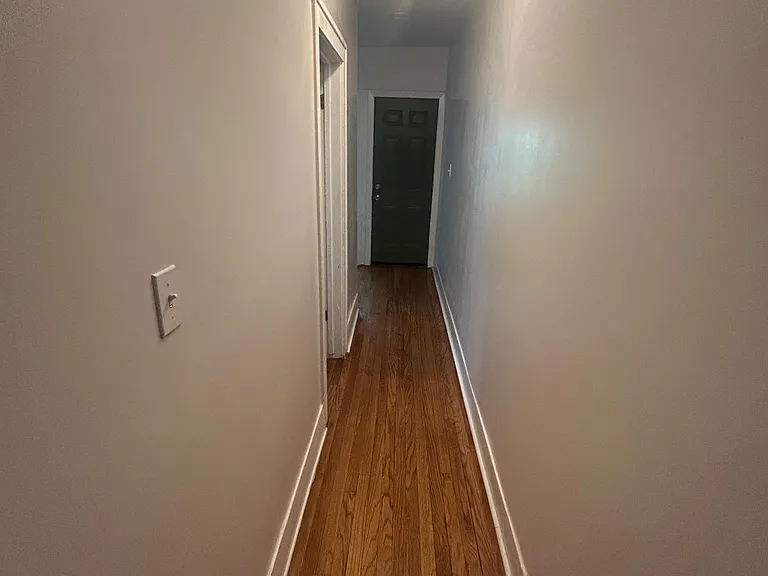 Long interior hallway with hardwood floors, smooth walls, and overhead lighting connecting rooms to the entry door.