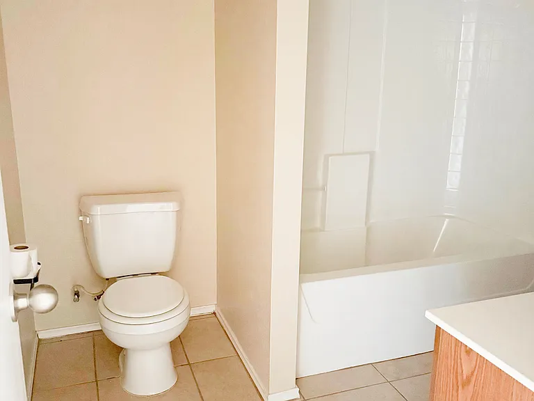 The hall bathroom toilet and bathtub/shower across from the sink and cabinets.