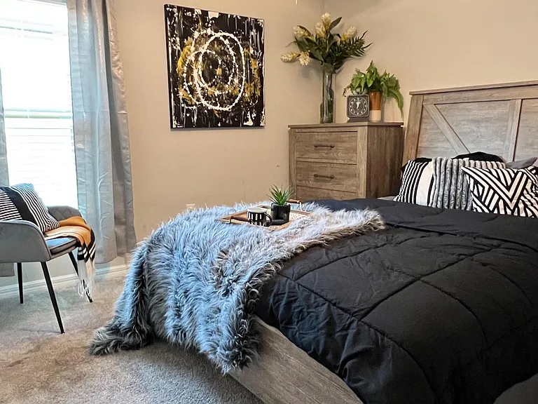 Well-furnished bedroom with a queen bed, dresser storage, and a window seating nook with soft carpet underfoot.