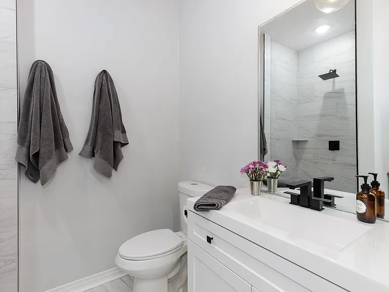 Airy bathroom with modern fixtures, abundant storage, excellent lighting, large vanity and tall mirrors.