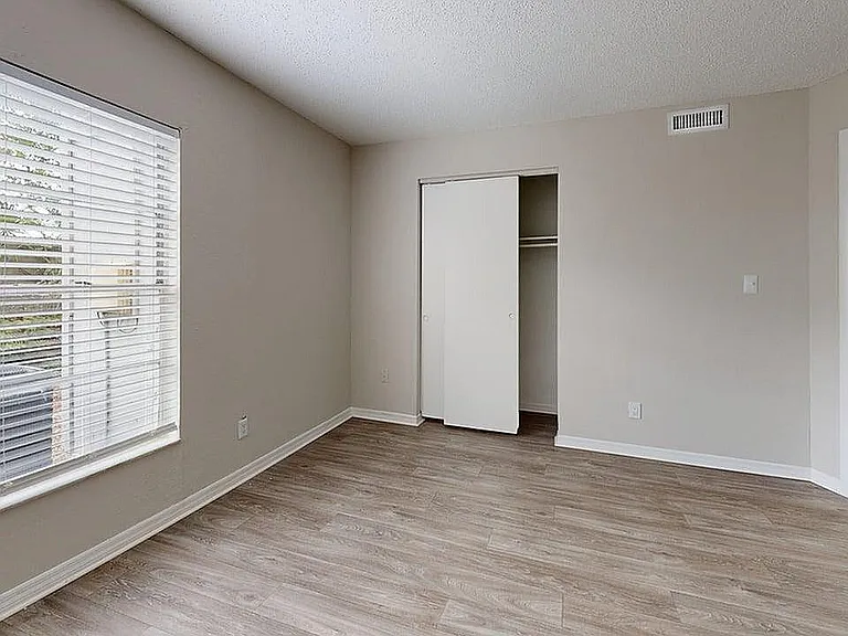 Bright room with large window, sleek hardwood flooring, and a spacious closet in a modern apartment.