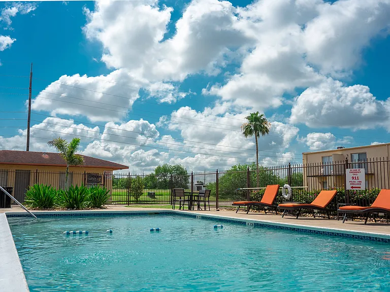 Refreshing outdoor pool with lounge seating and palm trees at Los Cedros Apartments in Brownsville, Texas.