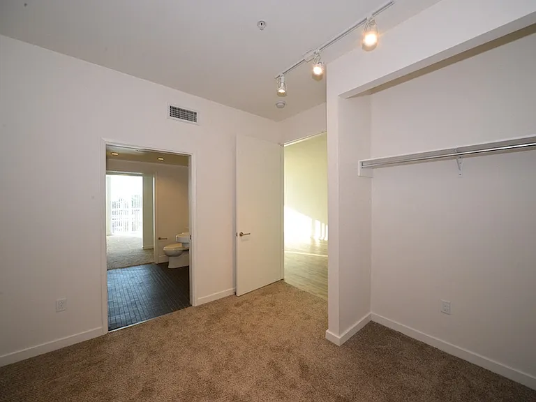 Carpeted bedroom with spacious closets and shared bathroom at 12th Street Lofts in National City, California.