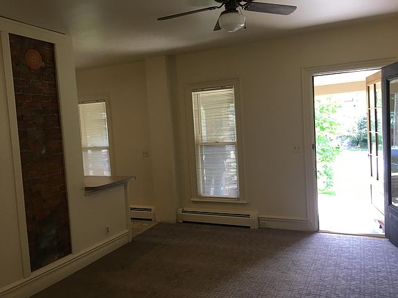 looking at living room to front wall. Kitchen is to left past the exposed chimney