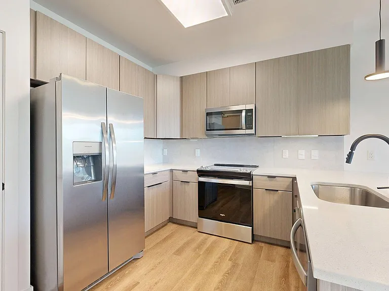Apartment kitchen with stainless steel appliances, light counters, and wood style floor.