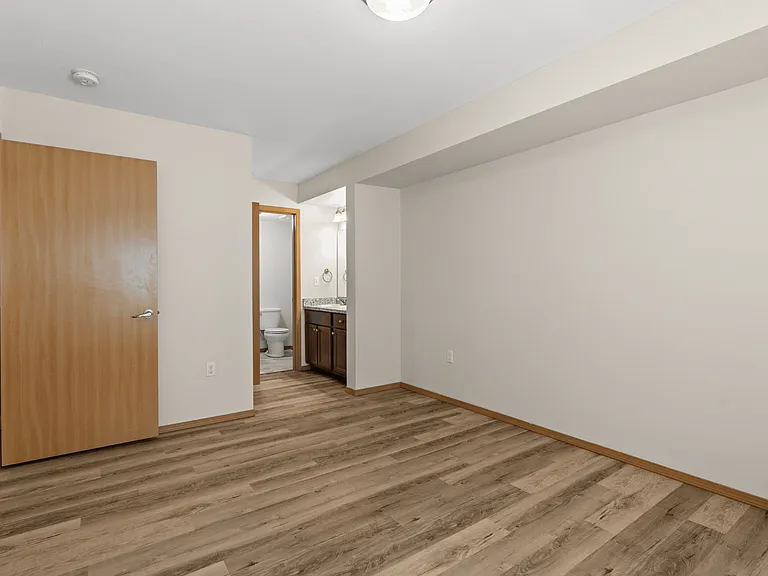 Spacious bedroom with wood-style flooring and nearby bath. Spacious bedroom with wood-style flooring and nearby bath.