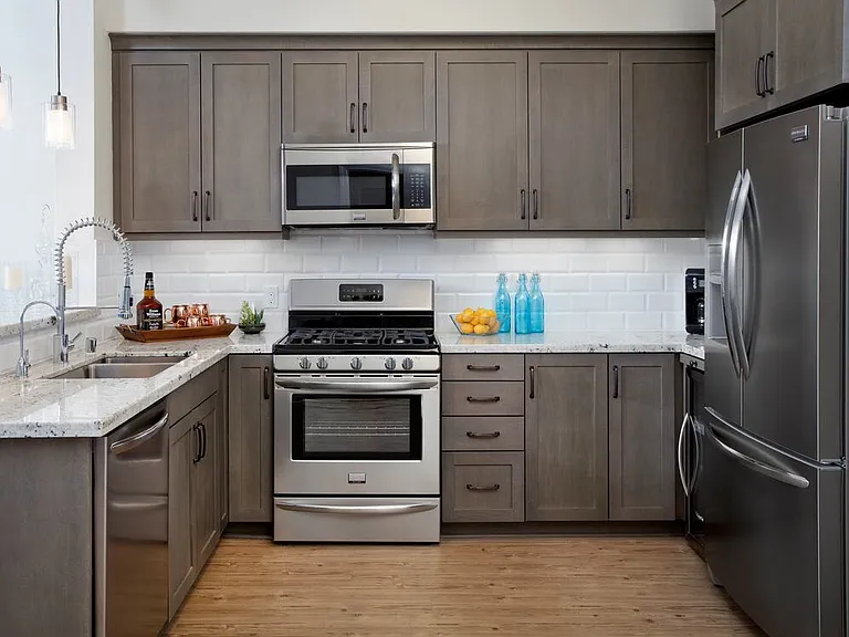 Kitchens with grey cabinetry, grey speckled granite countertops, white subway tile backsplash, stainless steel appliances, and hard surface flooring