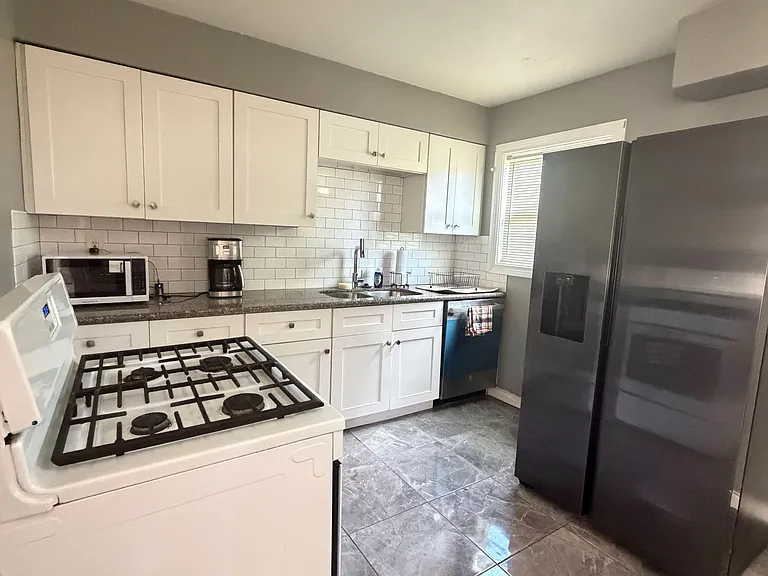 Efficient kitchen with ample cabinetry, tile backsplash, and full-size appliances including gas range and refrigerator.