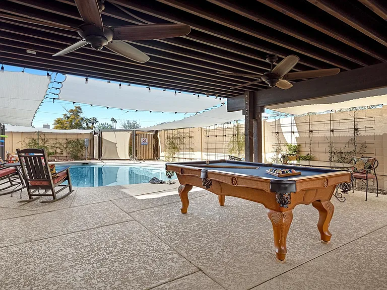 View off the backyard patio that showcases a pool table and large swimming pool with lots of space for entertaining.