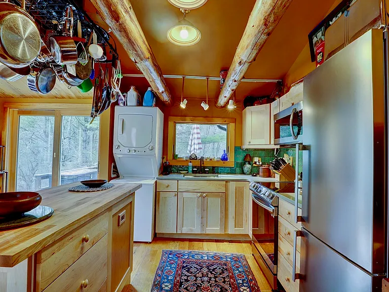 Kitchen Area with stacked washer / dryer, butcher block island with wrought iron pot rack, stainless steel sink with window, electric stove, microwave and refrigerator.
