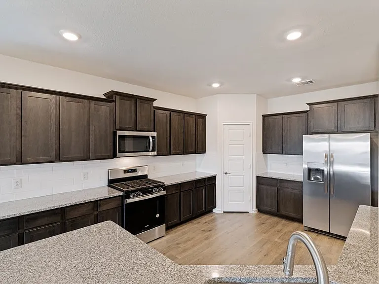 Kitchen featuring dark wood cabinetry, light-toned countertops, stainless steel appliances, a subway tile backsplash, and recessed lighting