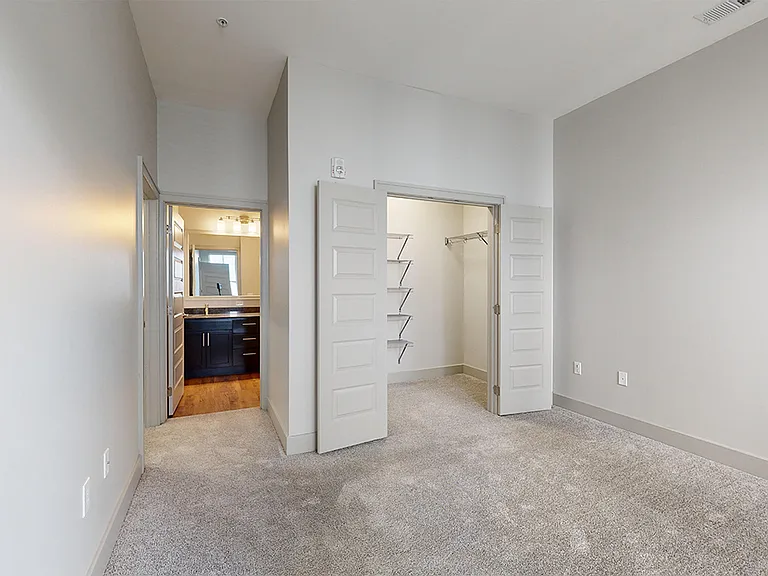 Spacious apartment bedroom with large closet, attached bathroom and plush carpet flooring.