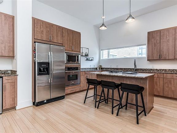 The Kitchen is a chef's dream with generous storage in warm stained cabinetry, granite countertops, & SS appliances. Island features gas cooktop with downdraft. Bar area on left has beverage chiller. All appliances including refrigerator, washer, & d