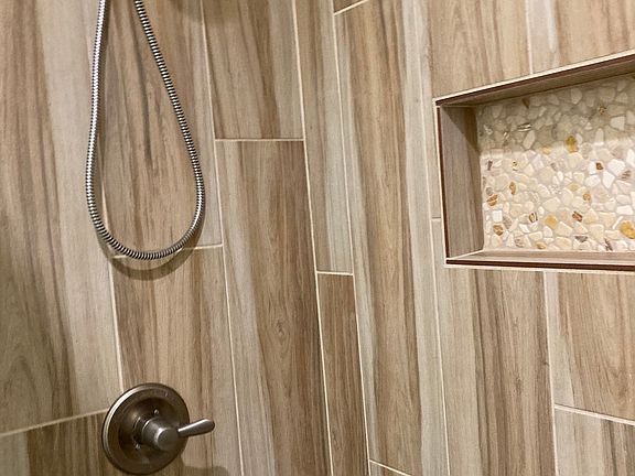 Shower in primary bathroom; also has double vanity, linen shelves, and privacy wall next to the toilet