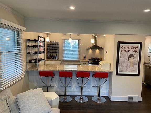 View through the chef's countertop passthrough into the kitchen. Recessed can lighting in the living room and kitchen ceiling. Pedestal lights accompany the granite countertop.