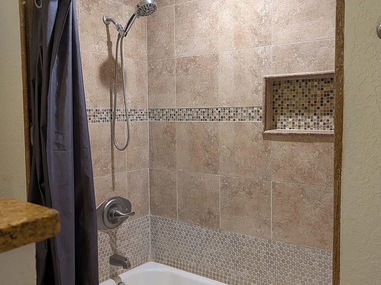 Tiled tub/shower combo with handheld showerhead and built-in niche, finished with mosaic accents for easy storage.