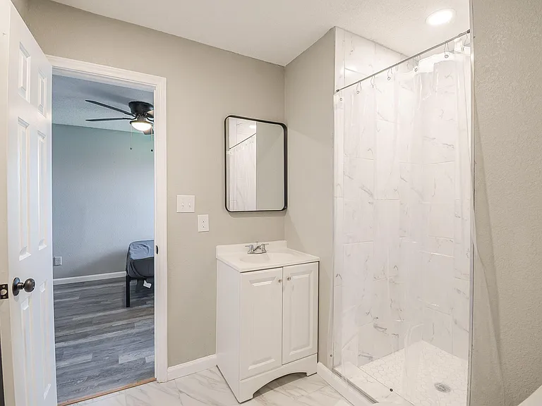 Clean full bathroom with a vanity sink, framed mirror, and shower/tub combo with tile-look surround for easy upkeep.