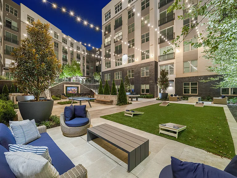 Chic apartment courtyard at night featuring cozy seating, lush greenery, and elegant string lights for a welcoming ambiance.